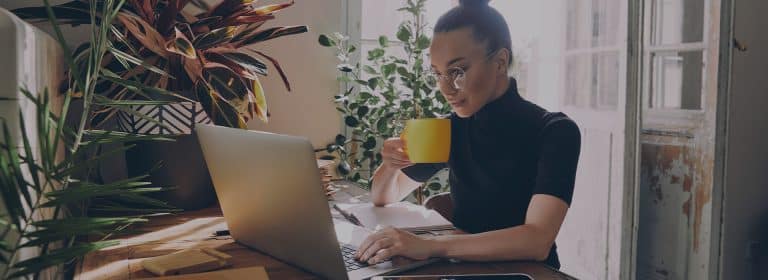 Frau sitzt mit Tasse vor einem Laptop